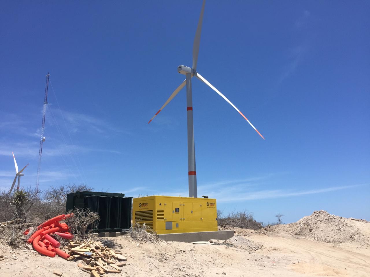 Una turbina eólica, un generador Genesal y un transformador negro en una zona árida de México.