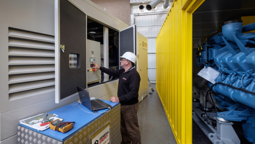 Genesal Energy technician inspecting and adjusting the control panel of an industrial generator set.