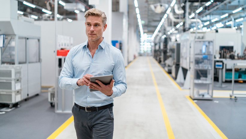 Industrial supervisor walking through a production plant with a tablet in hand for operational control and management.