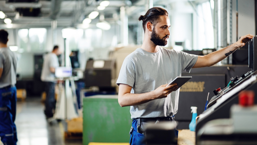 Technician overseeing industrial machinery with a tablet in hand for monitoring and control tasks in the plant.